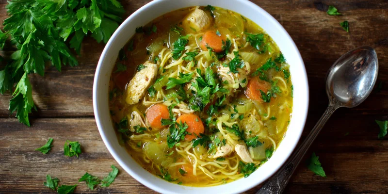 Vegan chicken noodle soup recipe with carrots and herbs in a white bowl